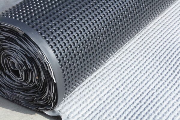 ​Rollo de lámina drenante Atus Silkworm de 8 mm con geotextil blanco, desplegado sobre superficie de obra.